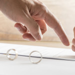 Male hand pointing to a divorce paper on which a woman is busy writing with a pen in a close up conceptual view.